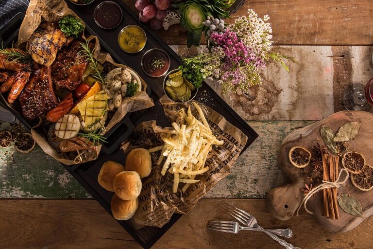 Gevarieerd diner op houten tafel Gevarieerd en kleurrijk diner met vlees, gegrilde groenten, friet en broodjes, typerend voor de moderne foodsector.