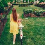 Vrouw in gele jurk met fiets wandelt door een groene tuin vol bloemen, onderdeel van haar ondersteunende omgeving.