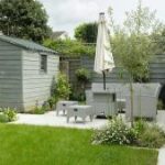 Rustige tuin met houten tuinhuis, zitplek met lichtgrijze tuinmeubels en groene beplanting