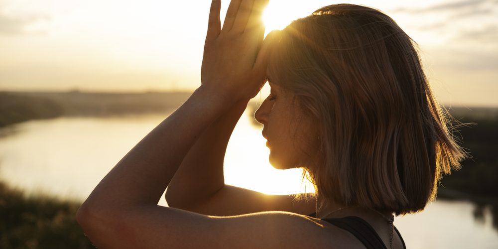 Vrouw in meditatieve houding bij zonsondergang als beeld van energiehealing en een eerste Magnified Healing-sessie.