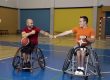 Twee mensen in sportrolstoelen met een basketbal in een sporthal.