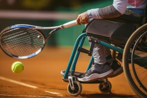 Rolstoeltennis speler slaat een tennisbal op een gravel tennisbaan.