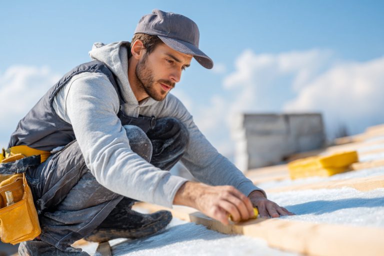 Dakdekker aan het werk Vakman brengt isolatiemateriaal aan voor een goed geïsoleerd dak tijdens renovatiewerkzaamheden.