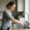 Vrouw houdt haar onderarm onder stromend kraanwater in de keuken om een verbrande huid te koelen